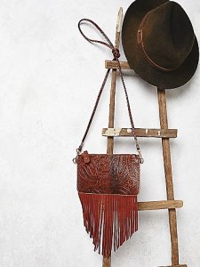 Beautifully tooled vegan leather crossbody featuring vegan suede fringe accents. Long strap is removable and turns the bag into a clutch or wristlet. Zipper closure. 